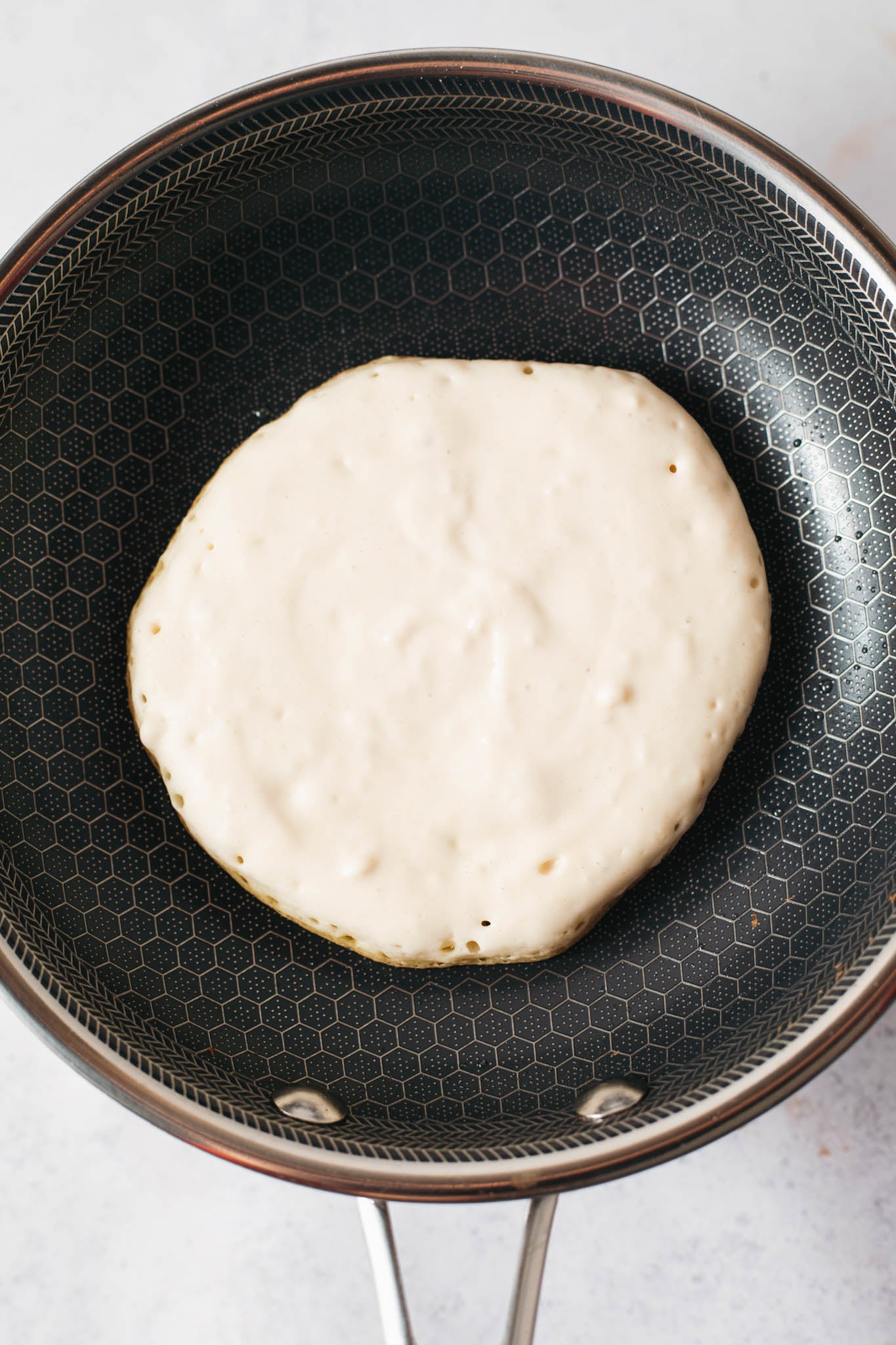 buttermilk pancake cooked on one side in a pan, ready to be flipped