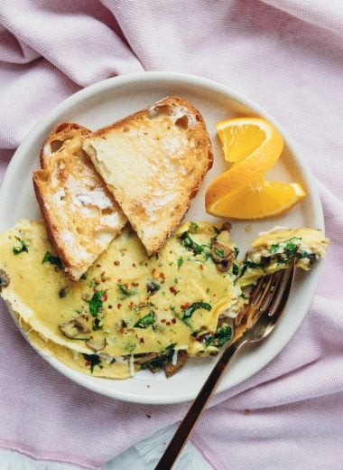overhead of a vegan vegetable omelette, buttered sour bread toast and an orange wedge on a white plate.