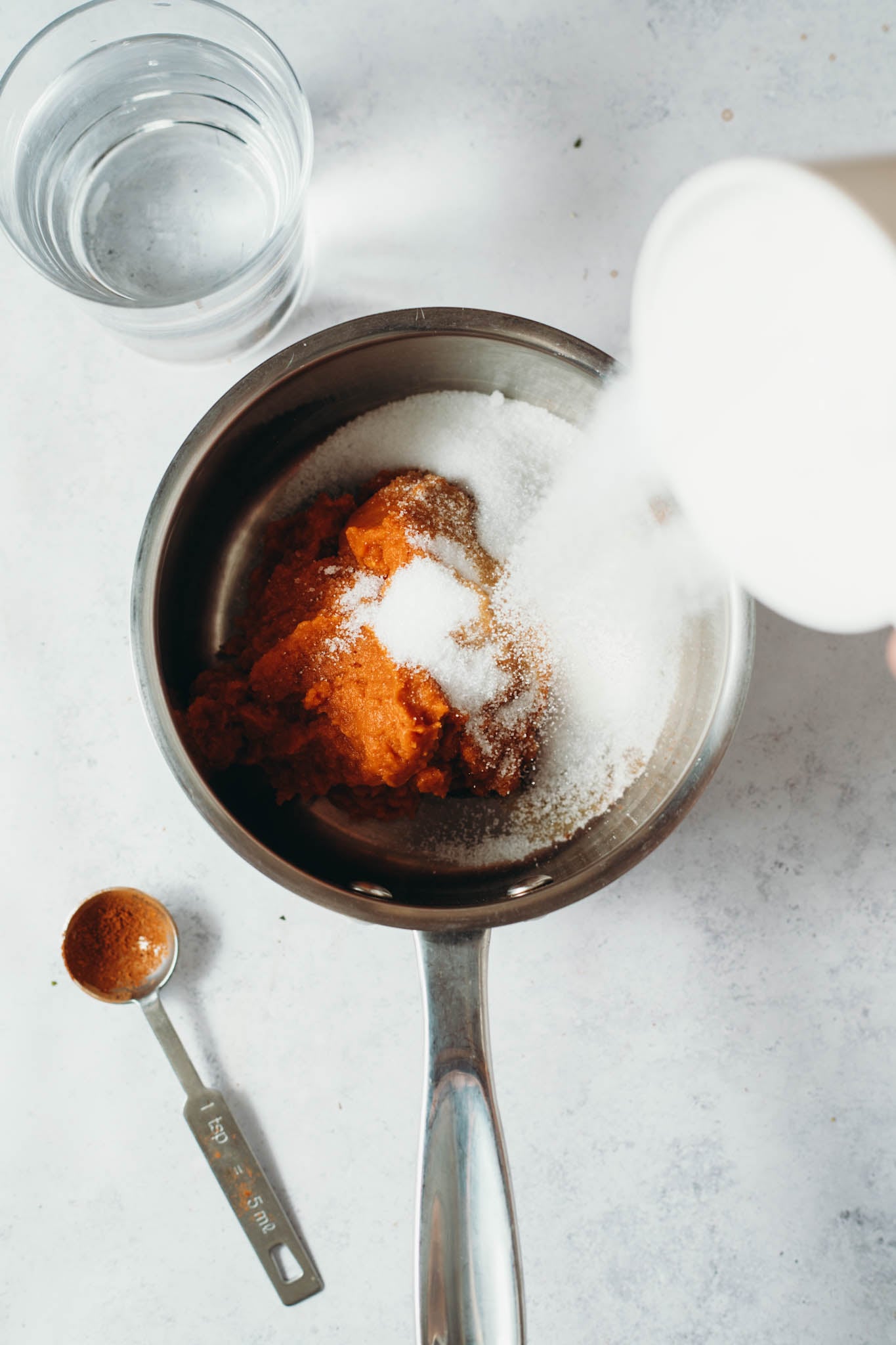 sugar being poured into a pot with pumpkin sauce mixture to form a syrup.