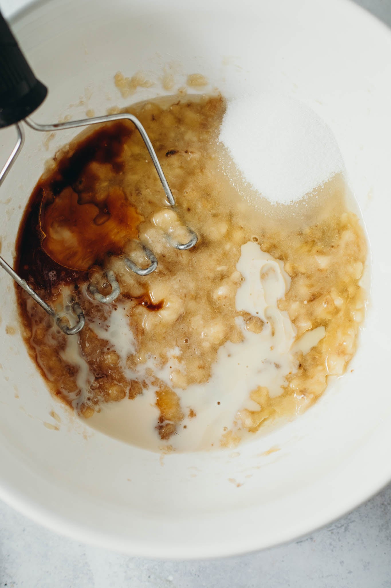 overhead view of ingredients being poured into a large white bowl to make vegan chocolate banana bread