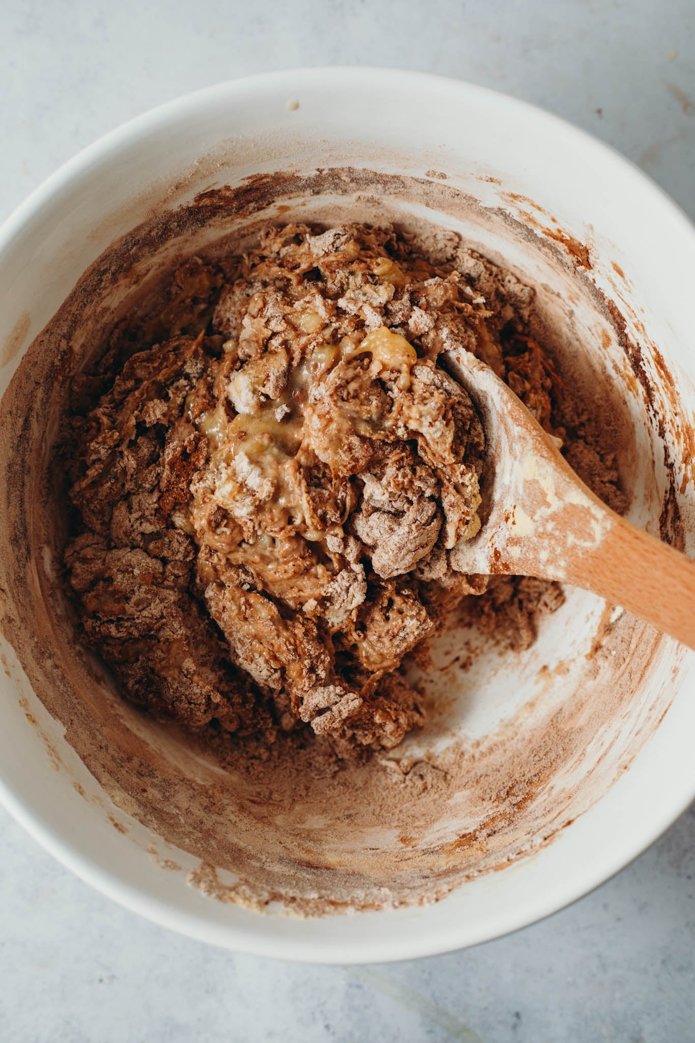 ingredients being mixed into a large white bowl to make the dough for vegan chocolate banana bread with protein