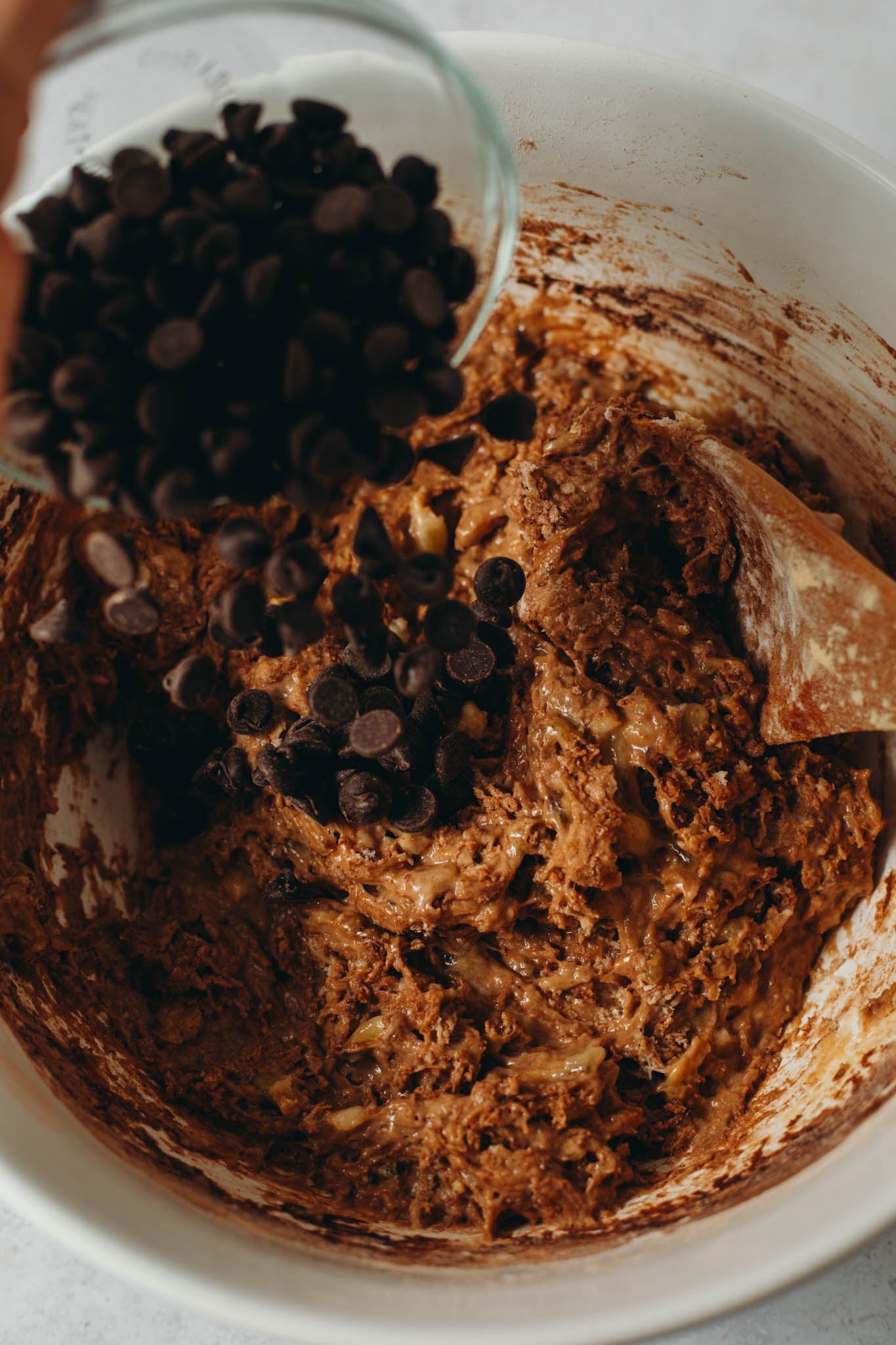 overhead view of chocolate chips being poured into the dough mixture for vegan chocolate banana bread in a large white bowl.