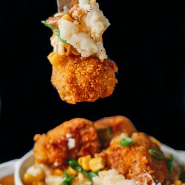 front on look of a pile of mashes potatoes, gravy, corn and vegan fried chicken bites in a white oven baking dish with a fork overtop displaying each of the components