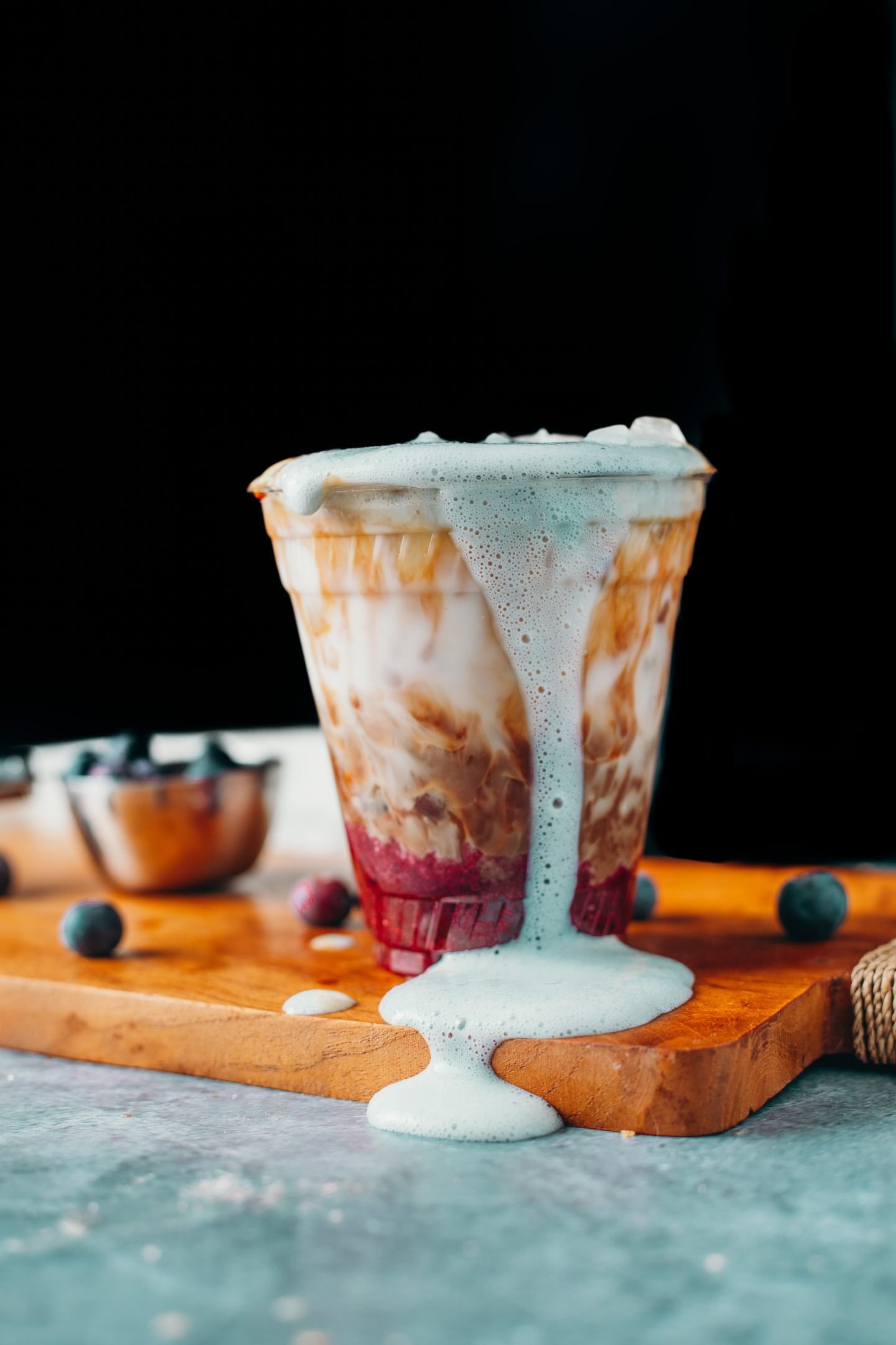 a purple collared simple syrup blueberry bottom layer, topped with a swirl of espresso and milk, ice and blue coloured cold foam dripping down the front of the plastic cup