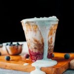 a purple coloured simple syrup blueberry bottom layer, topped with a swirl of espresso and milk, ice and blue coloured cold foam dripping down the front of the plastic cup