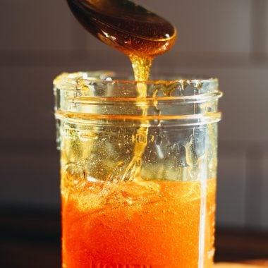 side photo of vegan honey in a sunbeam with spoon dipping into it.