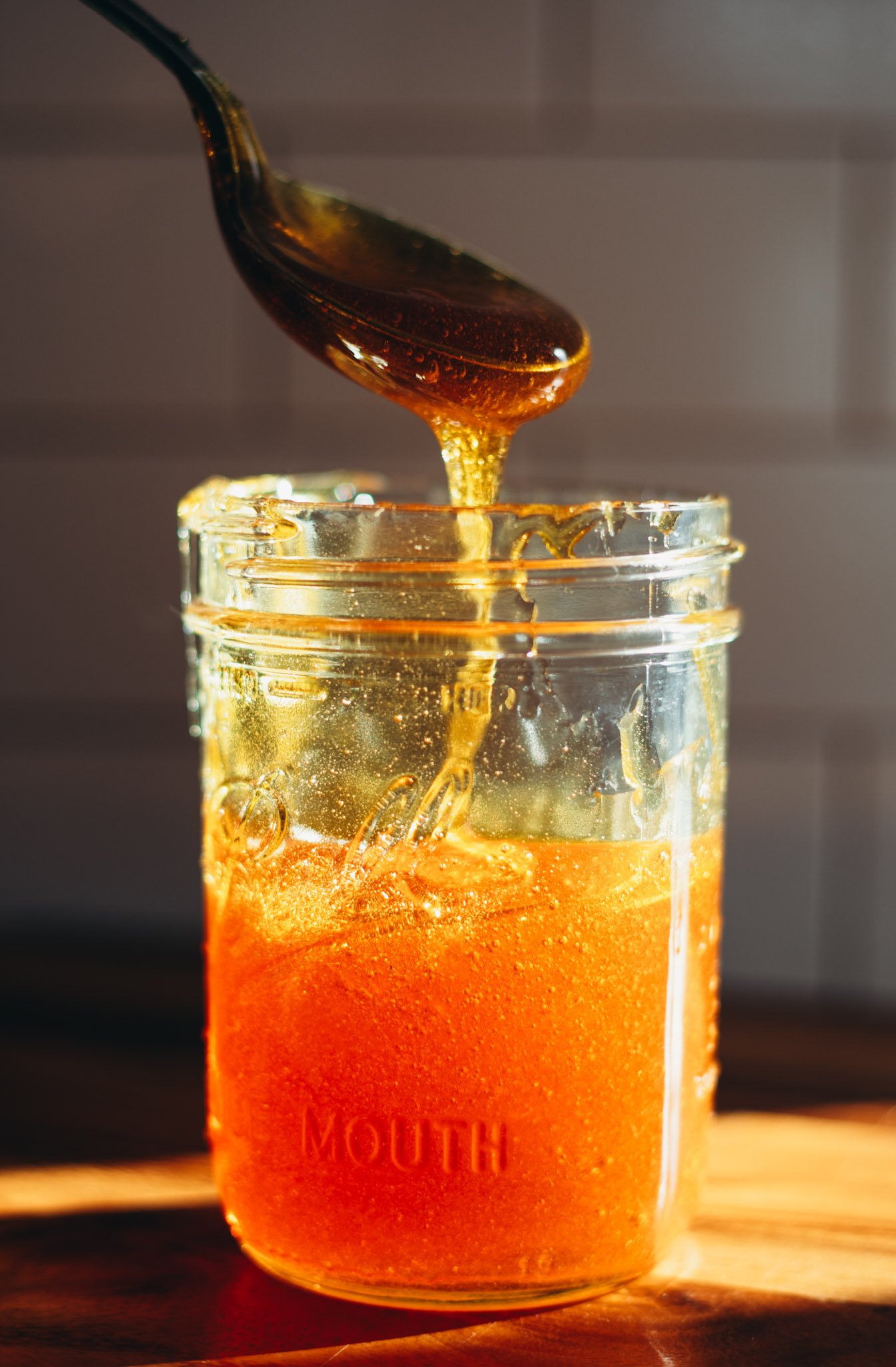 side photo of vegan honey in a sunbeam with spoon dipping into it.