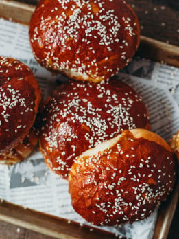 overhead view of large golden burger buns on a baking sheet with sesame seed topping