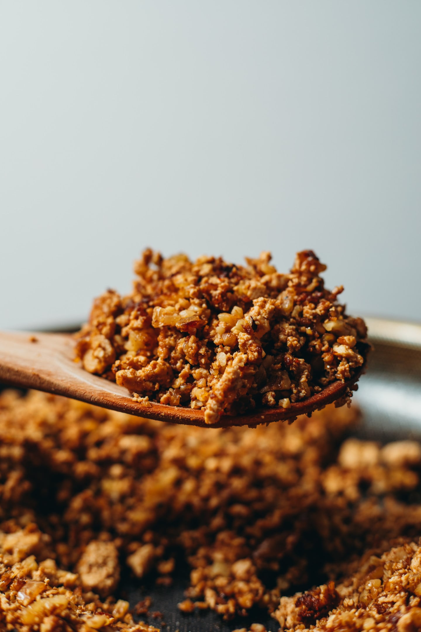 side view of taco meat lifted on a wooden spoon from a black pan over a white background.