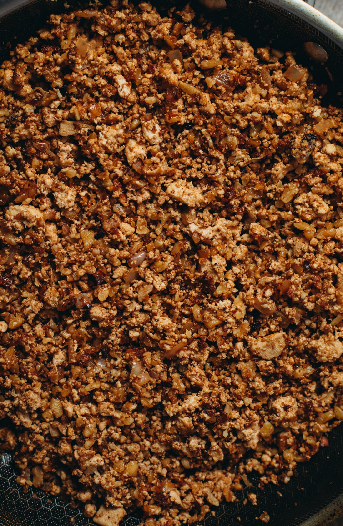 Overhead view of a the taco beef in a black pan on brown board background.