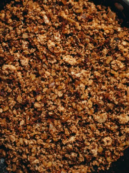 Overhead view of a the taco beef in a black pan on brown board background.