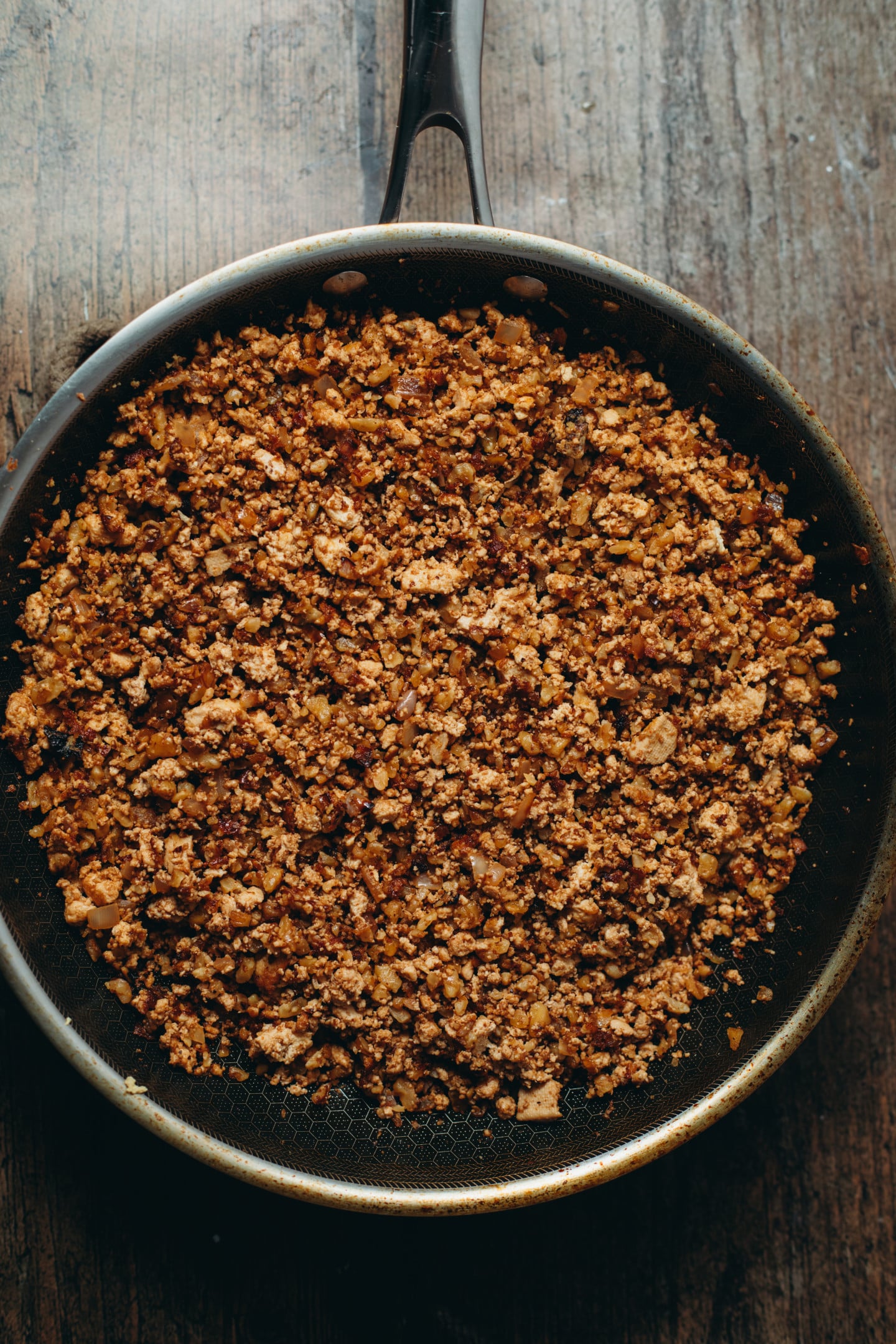Overhead view of a the taco beef in a black pan on brown board background.