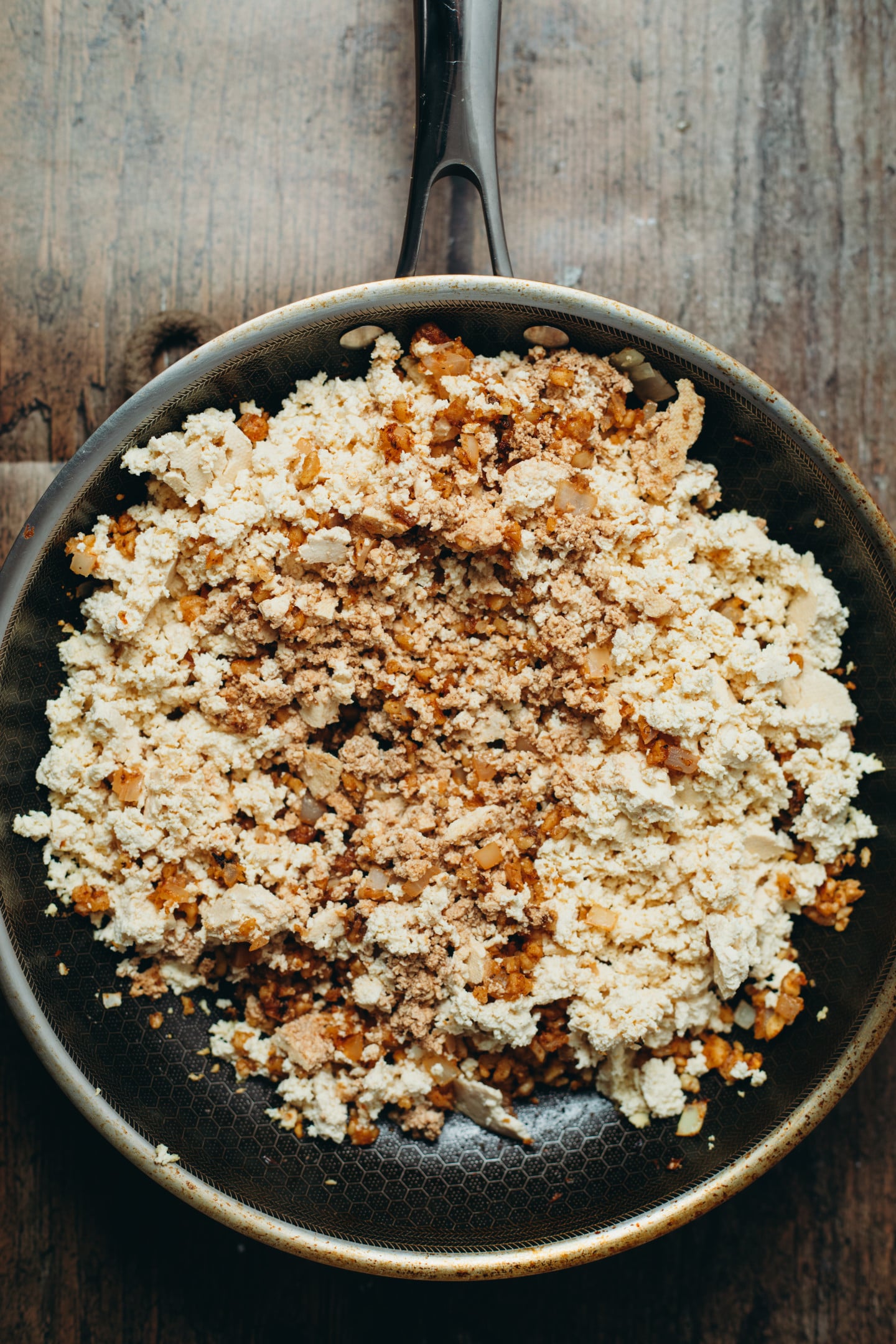 Overhead view of a the pre-cooked taco beef in a black pan on brown board background.